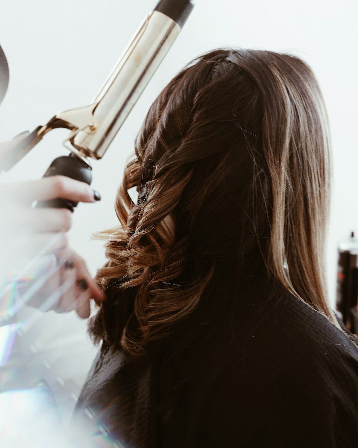 Stylist curling a client's long brown hair