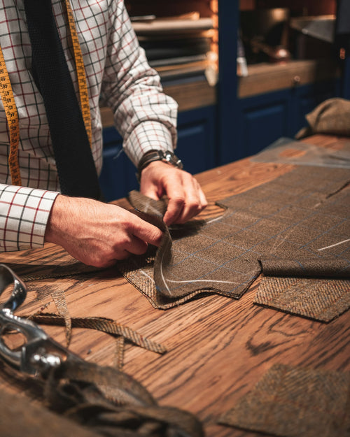 A tailor works suit fabric on a wooden cutting table
