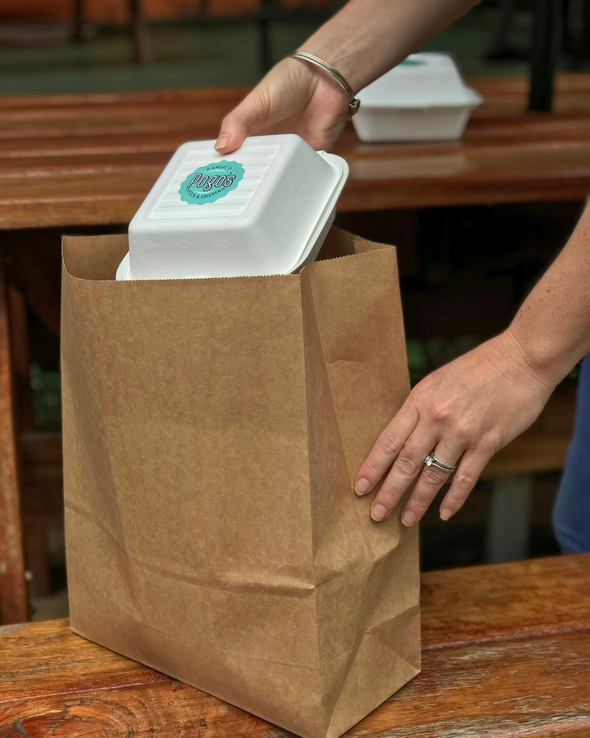 Hands packing a takeaway box into a kraft paper bag