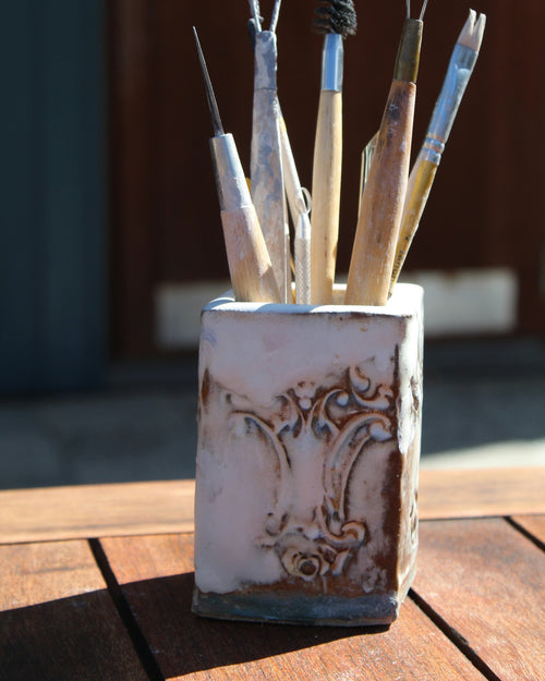 Pottery tools in a handmade ceramic cup on a wooden table