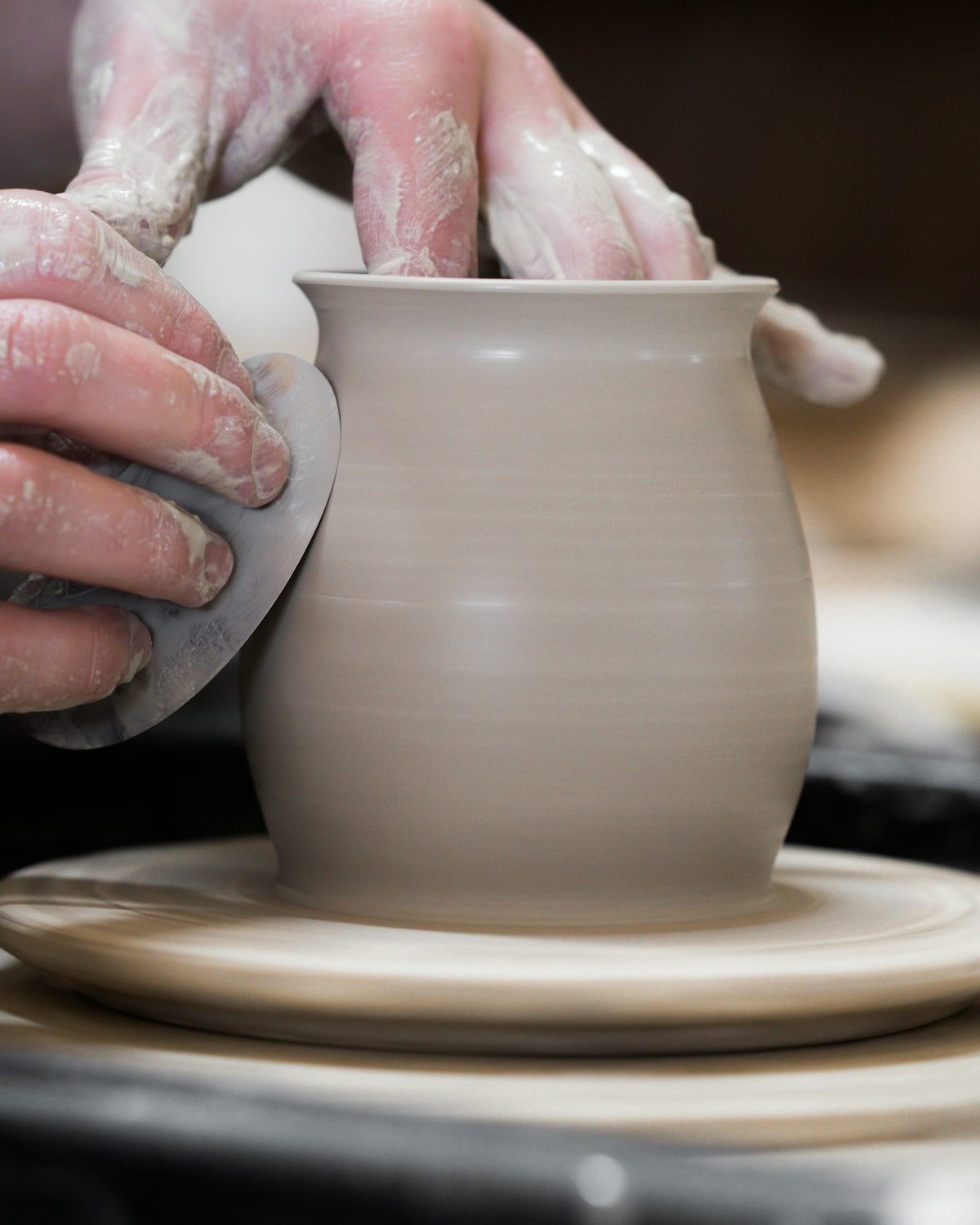 Hands shaping a clay vase on a pottery wheel