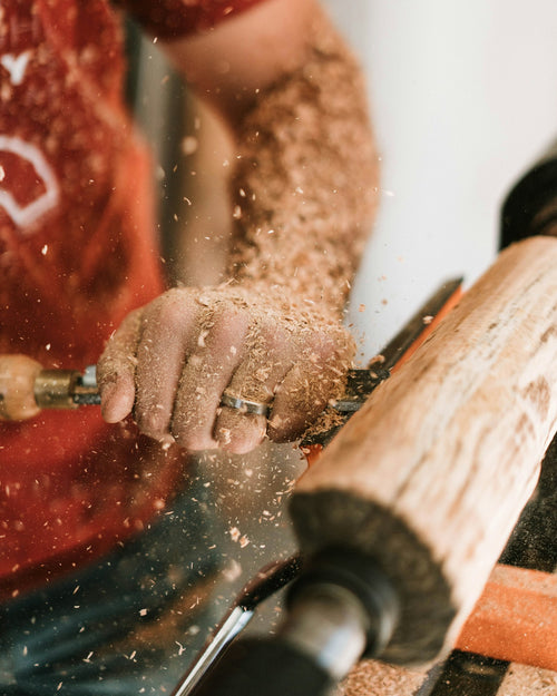 Hands shaping wood on a lathe as sawdust flies