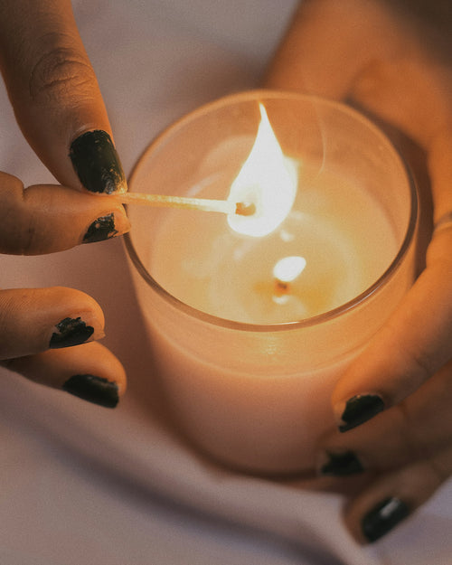 Hands lighting a handmade candle in a glass jar