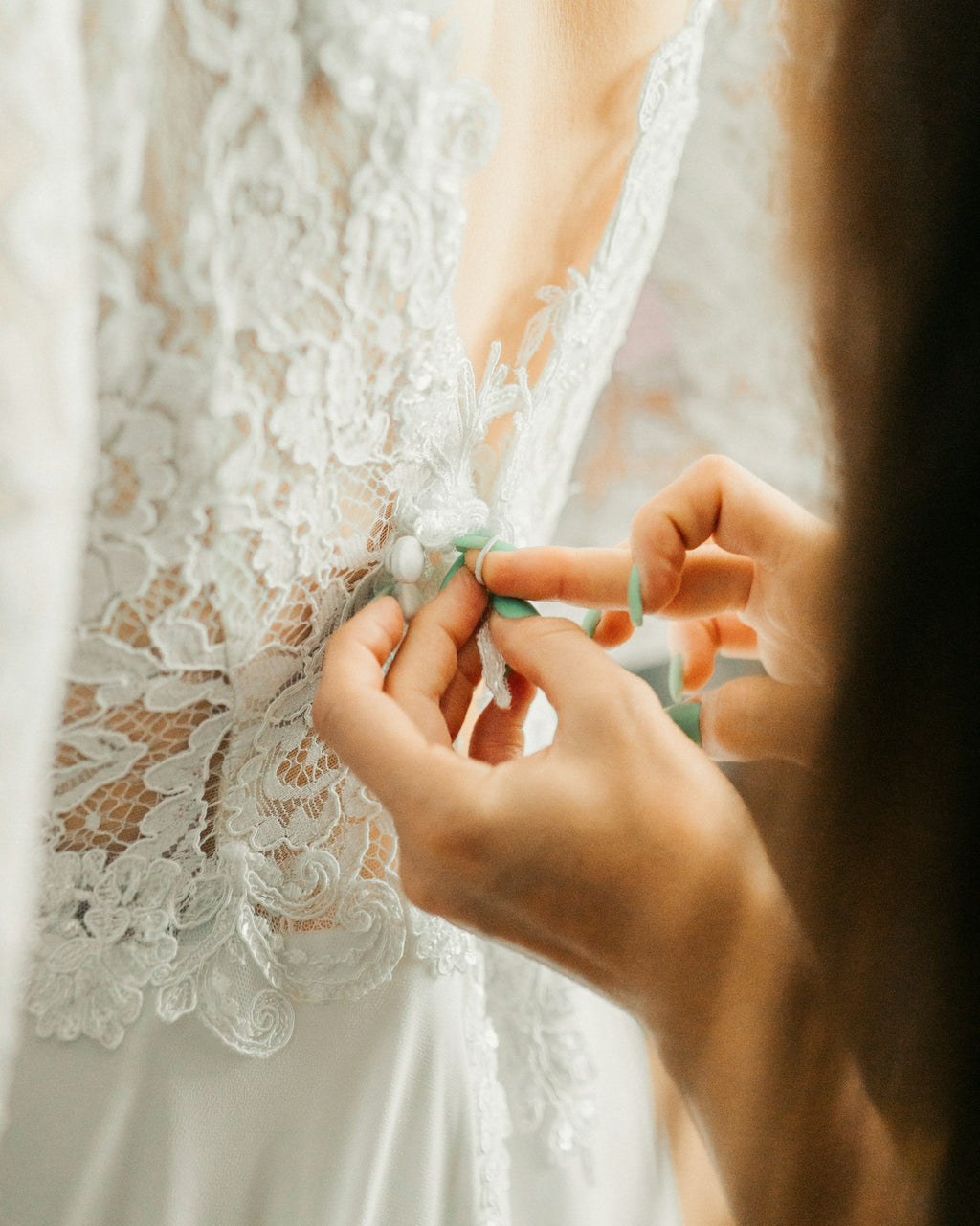 Tailor's hands fastening the lace back of a wedding dress