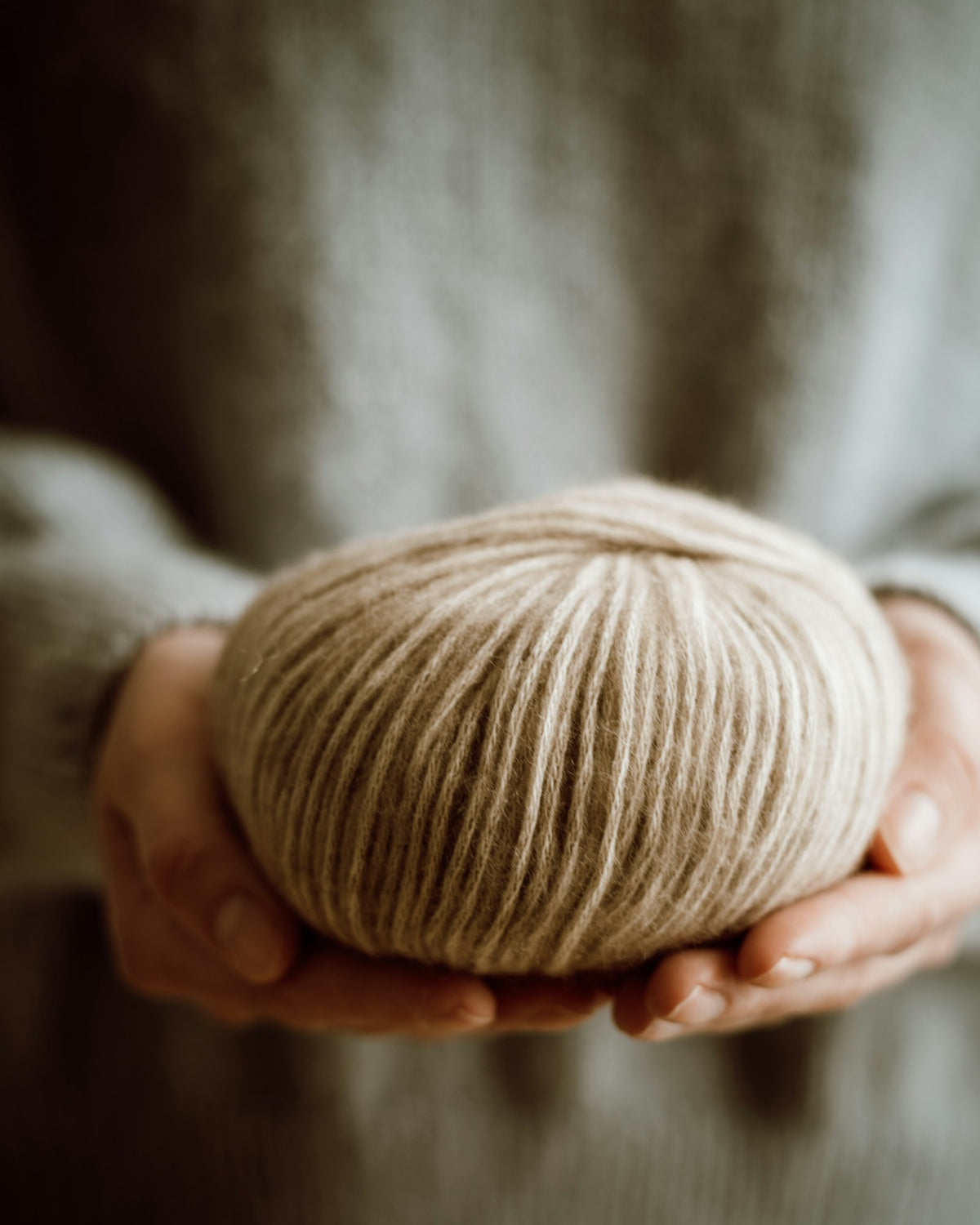 Hands holding a soft ball of undyed yarn