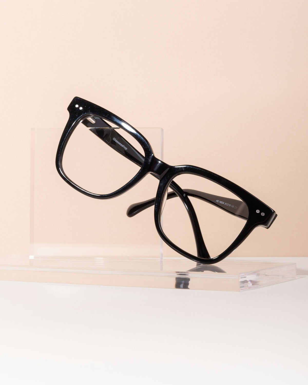 Eyeglass frames on a display stand against a beige wall
