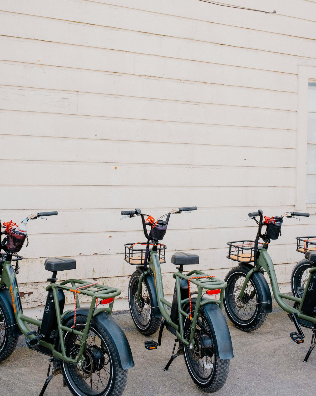 A row of sage green rental e-bikes against a white wall
