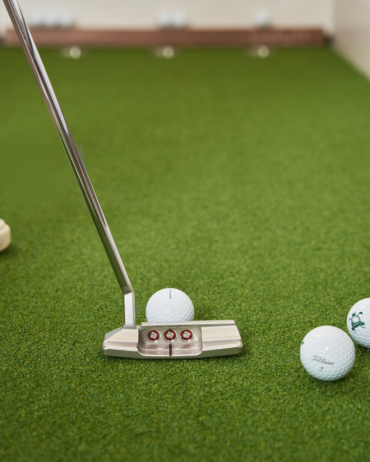 A putter lined up behind a golf ball on indoor turf